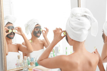 Young women with facial masks and cucumber slices in bathroom