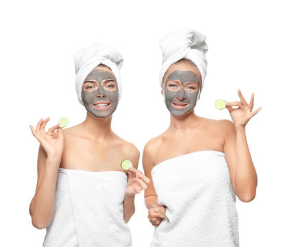 Young women with facial masks and cucumber slices on white background
