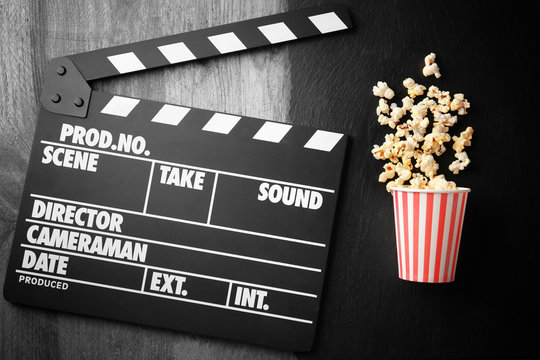 Paper cup with popcorn and movie clapper on wooden table