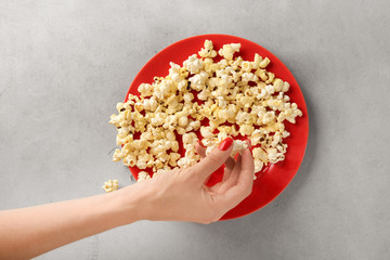 Woman taking popcorn from plate on table