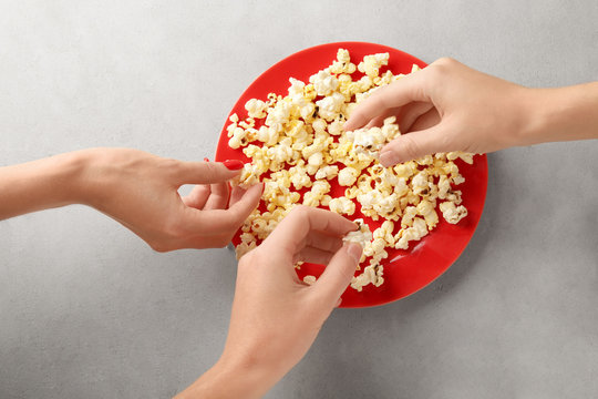 People taking popcorn from plate on table