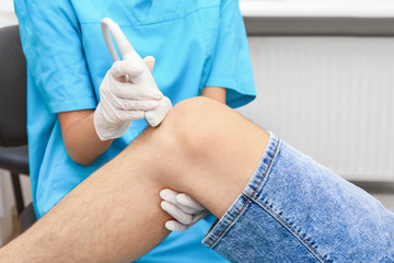Doctor conducting ultrasound examination of patient's knee in clinic