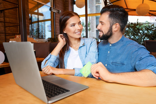 Young couple with laptop and credit card in cafe. Internet shopping concept