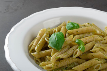 Pasta with homemade pesto sauce in a white plate on a dark stone slate background, closeup