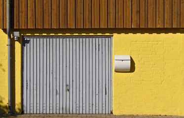 Yellow brick wall with garage door, mail box, downspout and wooden paneling on the second floor