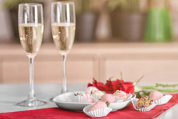 Plate with tasty glazed strawberries and glasses of champagne on table