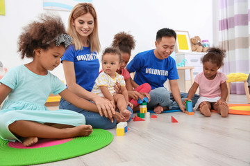 Young volunteers playing with little children in light room. Volunteering abroad concept