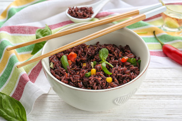 Bowl with red rice and vegetables on wooden table