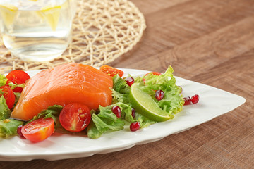 Plate with delicious salmon salad on table
