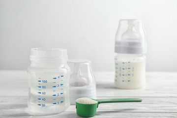 Bottle of water and powder for preparing baby milk formula on wooden table