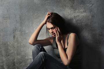 Battered young woman sitting near concrete wall