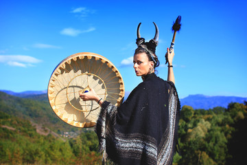 Tribal woman with horns playing a Buffalo drum on the mountain