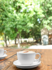 Cup of delicious coffee on wooden table outdoors