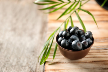 Bowl with fresh acai berries on wooden table, closeup