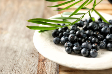 Plate with fresh acai berries on wooden table