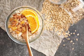 Tasty oatmeal with raisins and orange in glass on table