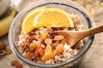Tasty oatmeal with raisins and orange in glass on table