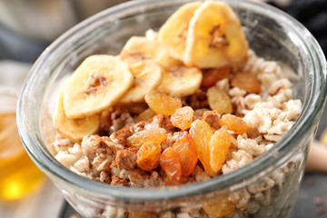 Nutritious oatmeal with banana and raisins in glass, close up