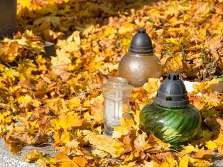 szklane znicze na grobie pokrytym jesiennymi liśćmi