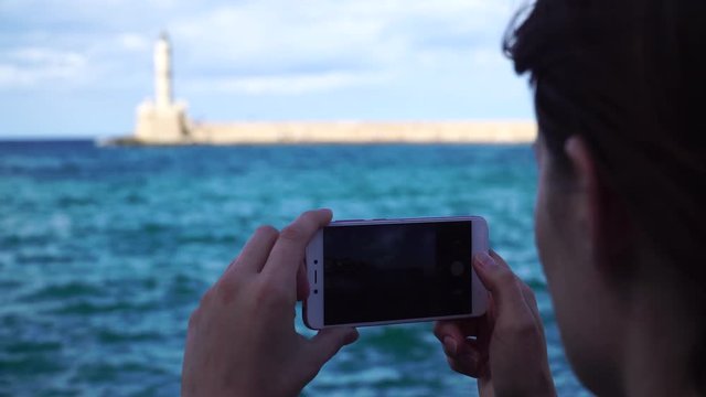 Young woman takes the photo a lighthouse in a European city uses smartphone