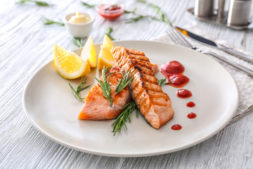 Plate with delicious slices of salmon and sauce on table