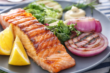 Slice of delicious salmon with vegetables on plate, close up