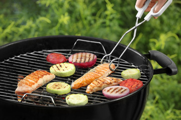 Woman cooking tasty salmon slices with vegetables on barbecue grill outdoors