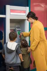 Mother and children withdrawing money from ATM machine.