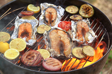Tasty salmon steaks with vegetables on barbecue grill, close up