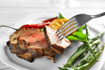 Fork with sliced delicious steak and vegetables on plate