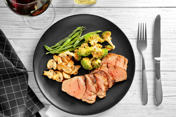 Plate with sliced delicious steak and vegetables on table