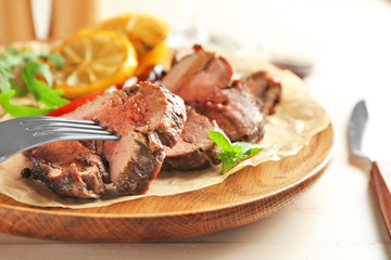 Fork and sliced tasty steak on wooden plate