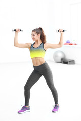 Fototapeta na wymiar Young sporty woman training with dumbbells in gym
