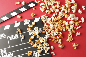 Tasty caramel popcorn and movie clapper on color background