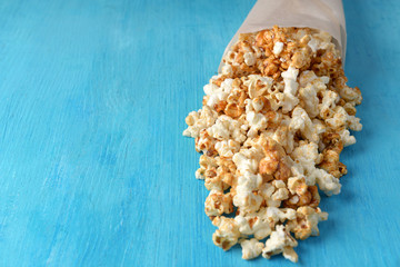 Paper cone with tasty caramel popcorn on color wooden background