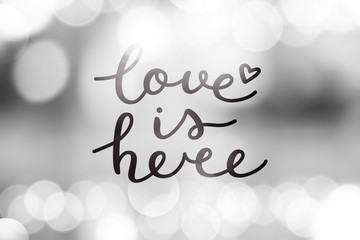 love is here lettering, vector handwritten text on blurred lights