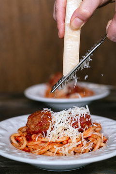 Food: grating Parmesan cheese on meatball pasta