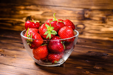 Ripe strawberries in glass bowl on wooden table