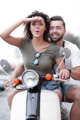 Beautiful young couple is smiling while riding a scooter