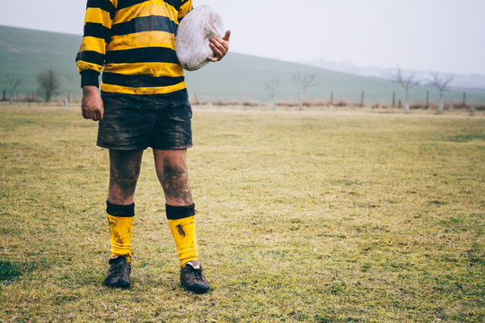 Muddy teenage rugby player holding a ball.
