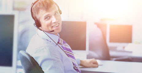 Happy young man working at callcenter, using headset