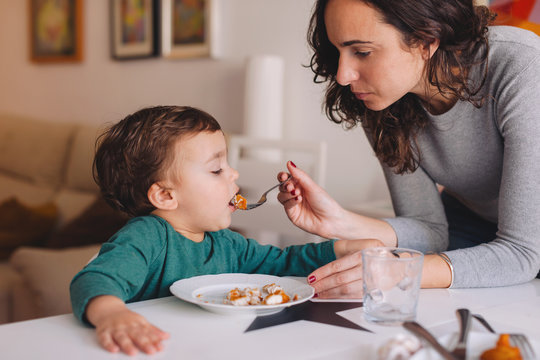 Mother helping her son to eat his meal.