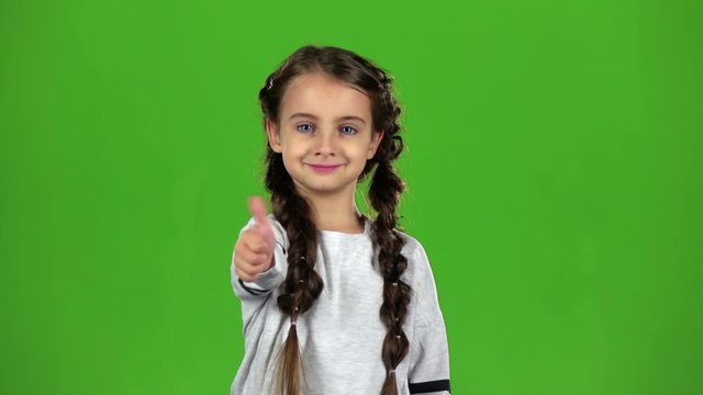 Child girl shows thumbs up. Green screen. Slow motion