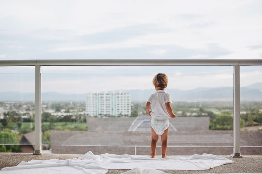 Cute toddler boy wearing diaper on balcony in summer morning