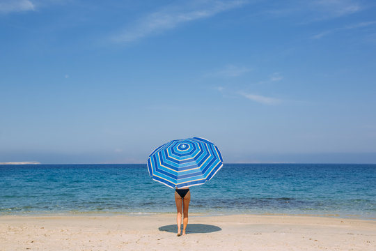 Woman walking with the beach umbrella to the sea