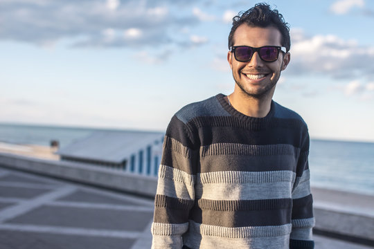 smiling handsome  Arabic young man in striped sweater on the sea coast, sunset,beach,clouds