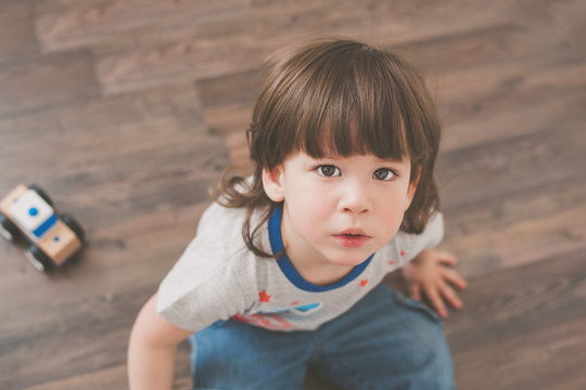 Cute little boy sitting on a wooden floor looking up with a serious face.