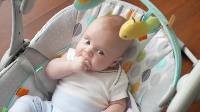 A small child sucks a finger. Toddler swings on an electric swing