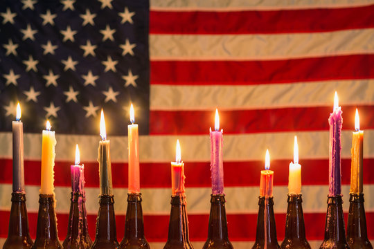 American flag illuminated by a row of candles in beer bottle holders
