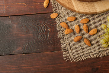 almond nuts and grapes at burlap tablecloth on old wooden texture background top view